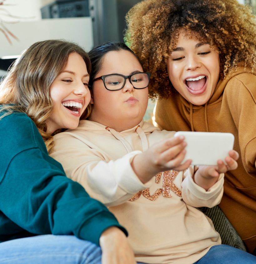 Two young women posing for a selfie with another young woman with Down Syndrome