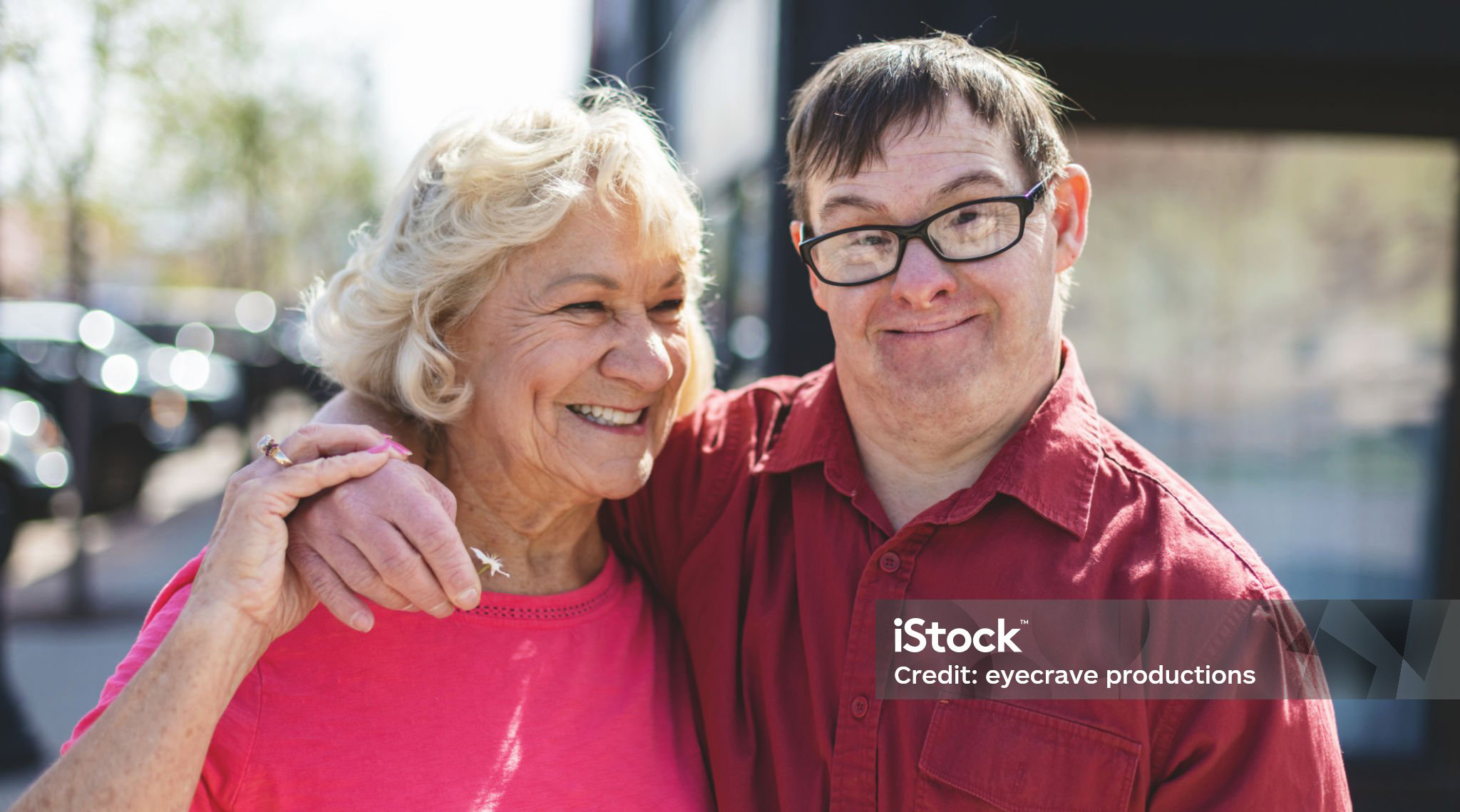 An older man with Down syndrome posing for a picture with his mother outside.