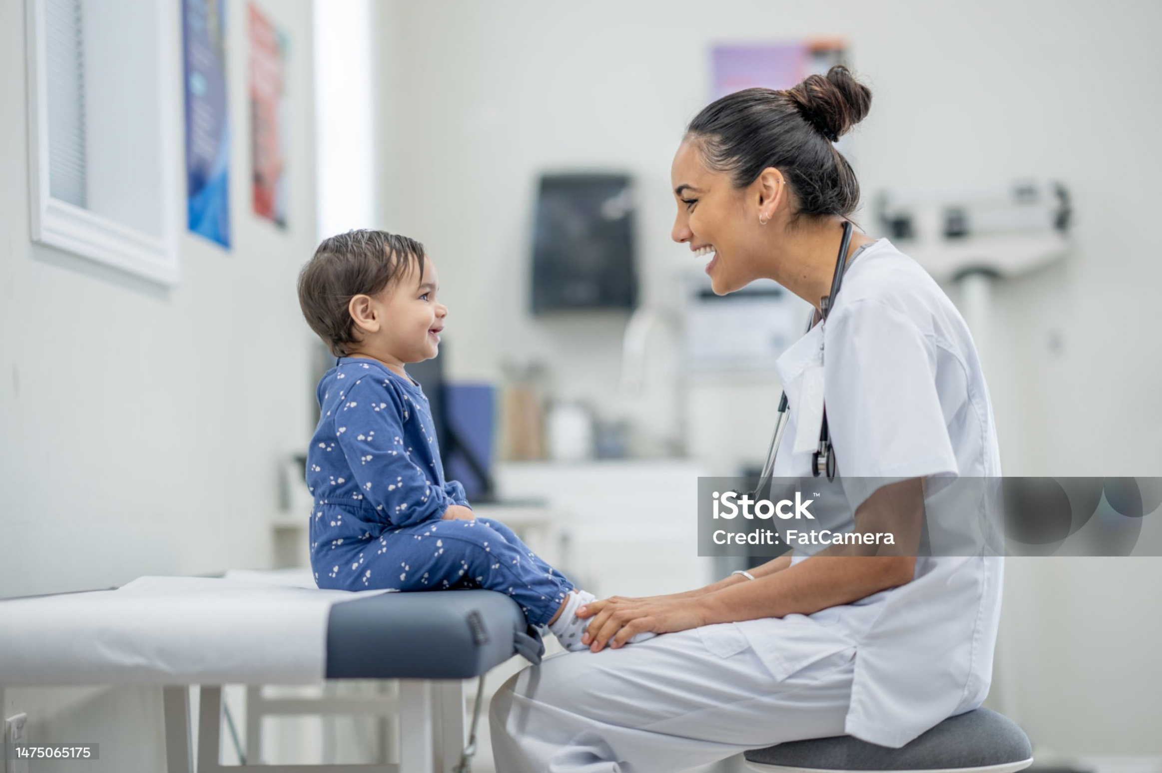 Happy toddler sitting on doctor's table smiling with female medical professional..