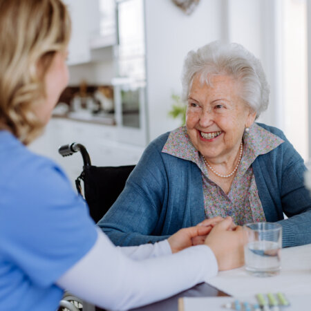 Caregiver supporting a smiling senior woman in her home.