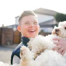 Boy with down syndrome laughing while holding a dog