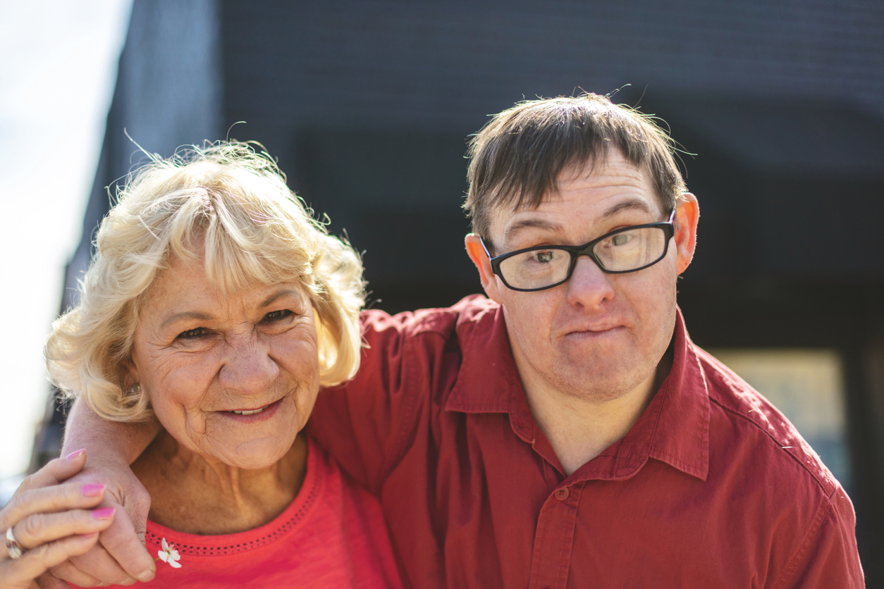 Adult man with Down Syndrome with arm around an older smiling woman