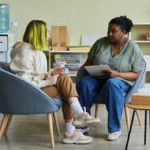 Female social worker talking to teenage girl while they sit on chairs at office.