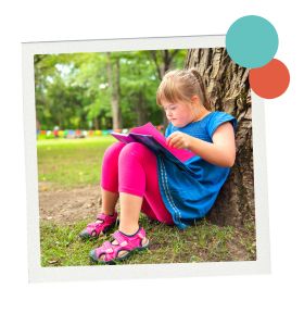 Young girl with Down syndrome reads a book outside