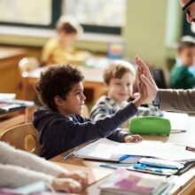 A teacher gives a high-five to a student in a classroom filled with kids