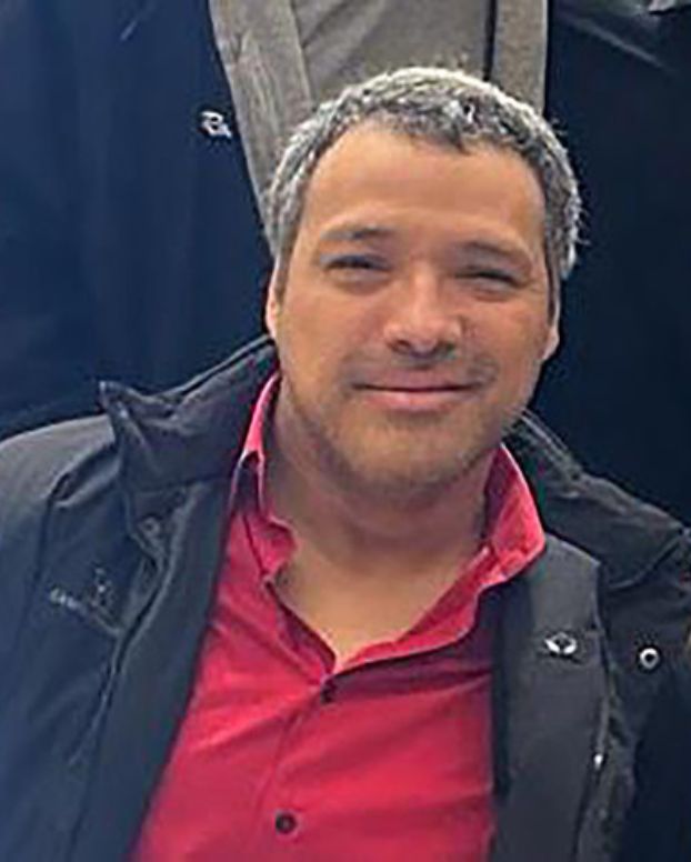 Man wearing a red shirt with black jacket smiles