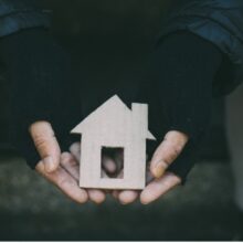 A person holding a small house figurine in their hands with a dark background