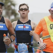 A group of men run an Iron Man triathlon together. One of the men has Down syndrome. Another man wears a shirt that says Guide