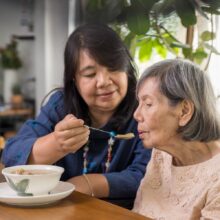 A family caregiver feeds an older adult woman soup