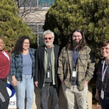 Five people from the Mission Supports Team at RMHS pose together in front of trees at the RMHS office in Denver